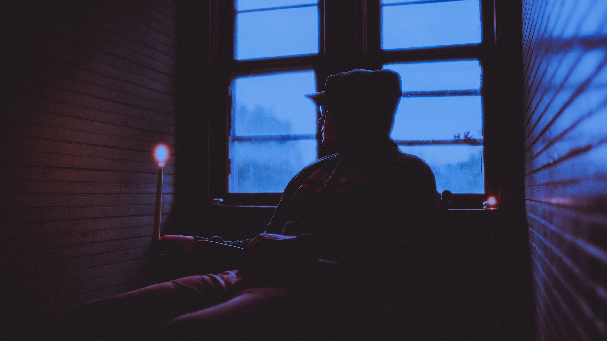 Cody Piper sitting in a dark room by a window with a candle